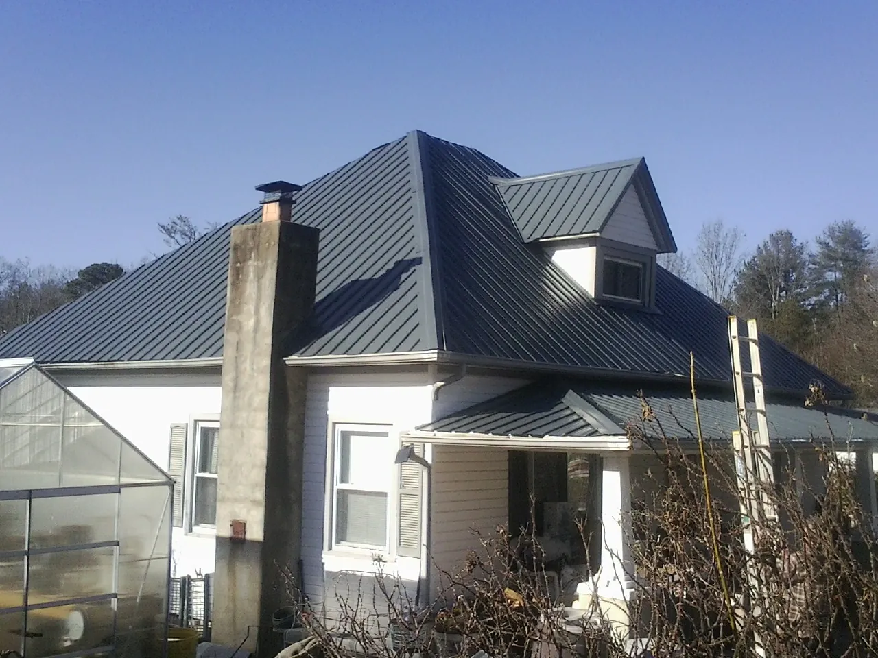 Dark blue standing seam metal roof on a white farmhouse with dormer — Slate & Tile Roof Repair by Roofing Brothers in Sheridan
